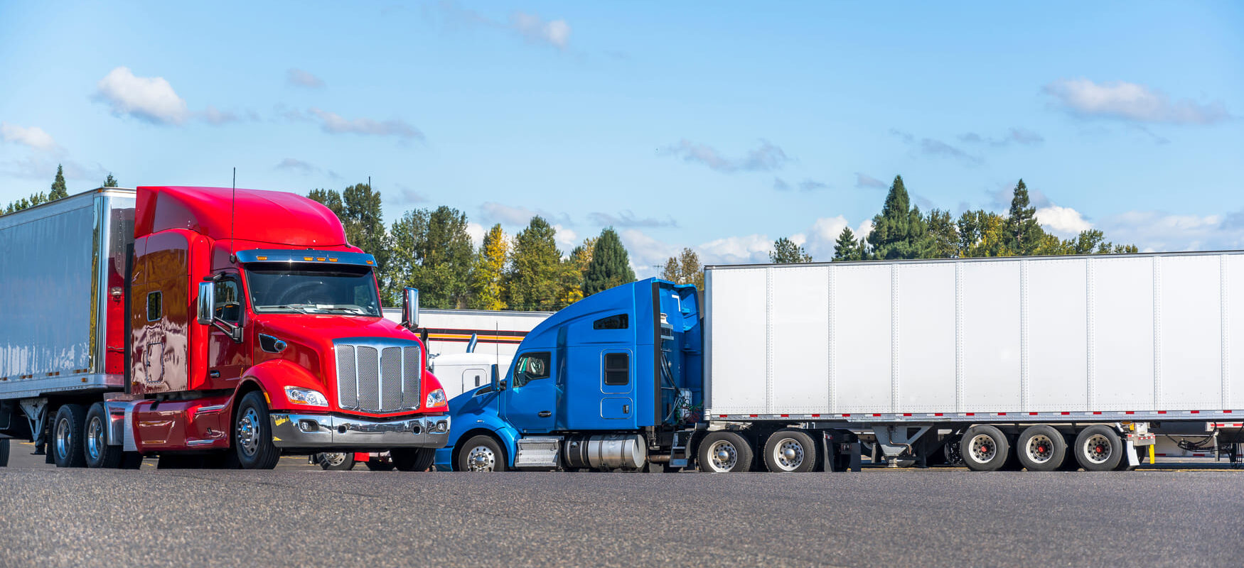 Red and blue semi-trucks parked at a logistics hub, representing full truckload and LTL freight shipping operations.