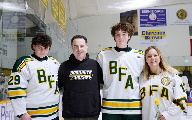 A father, mother, and their two sons in jerseys and a hoodie at a hockey game