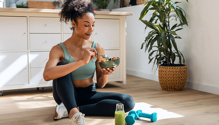 Athletic young woman eats fruit and exercises at home.
