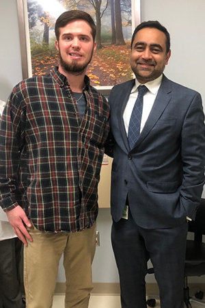 A male patient standing and smiling next to his doctor in wearing a suit.
