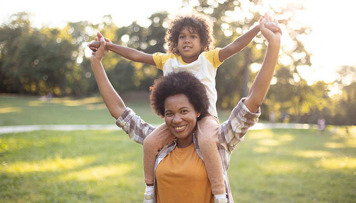 Woman walking in park with child on her shoulders