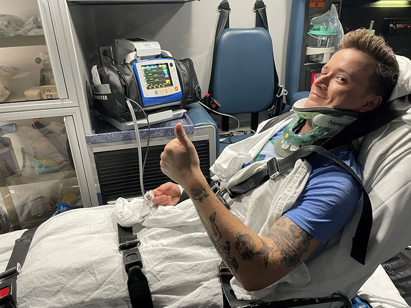 Gavin Davis giving a thumbs up while in a neck brace in the back of an ambulance