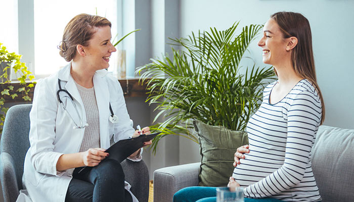 A smiling pregnant woman meets with her doctor to discuss lowering risk of birth defects.