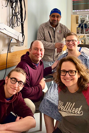 A male patient in a hospital room with his surgeon standing behind him and his support system of three people sitting the front with everyone smiling